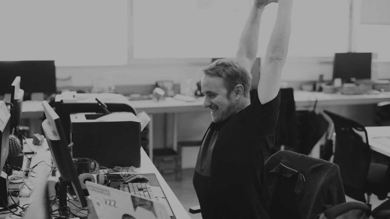 A man smiling and stretching at his desk